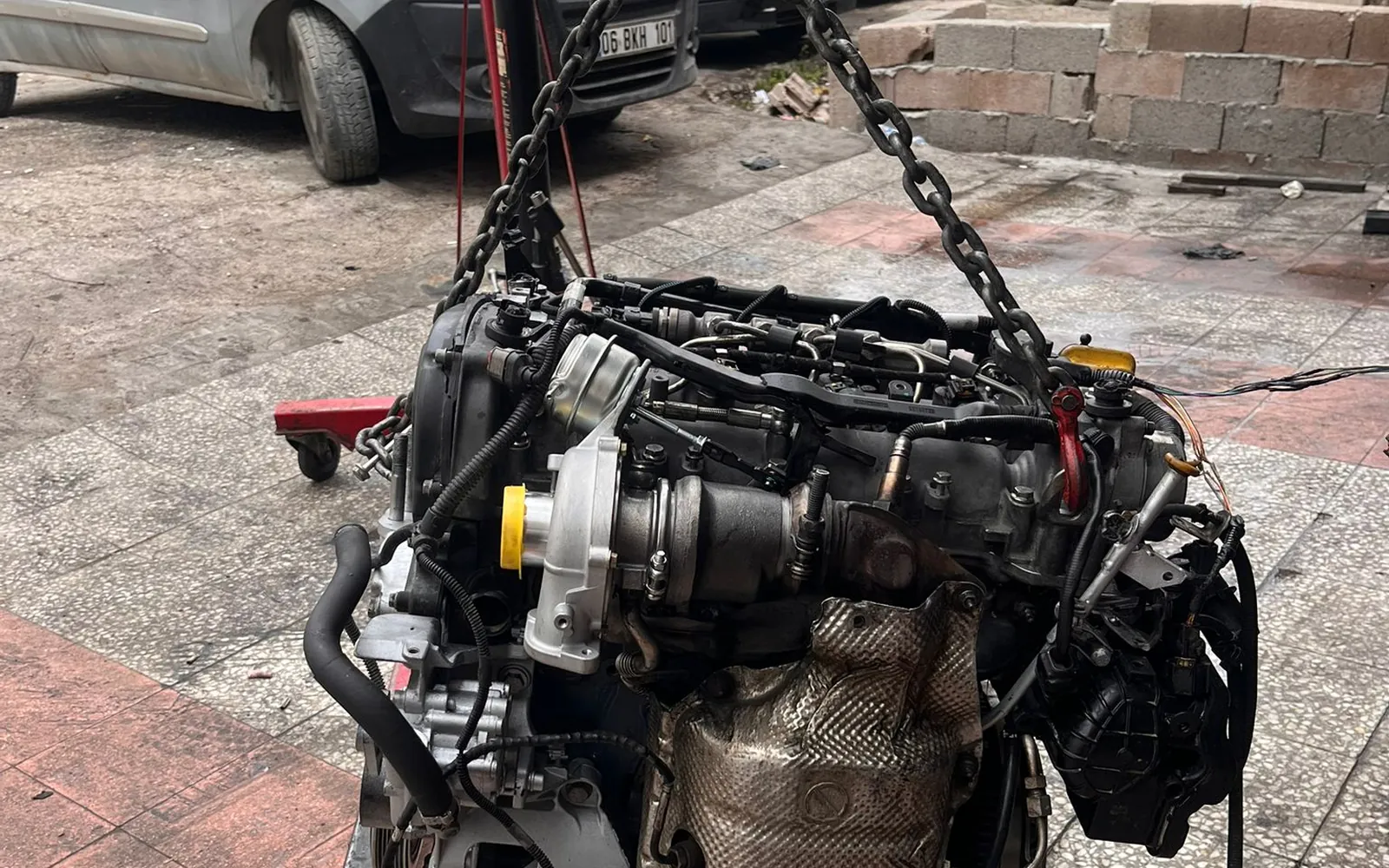 Turbo ve egzoz grubu görünür halde vinçle askıya alınmış motor, tamirhane önünde